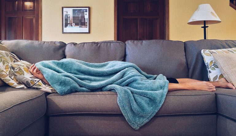 vrouw die misselijk op de bank ligt onder een deken