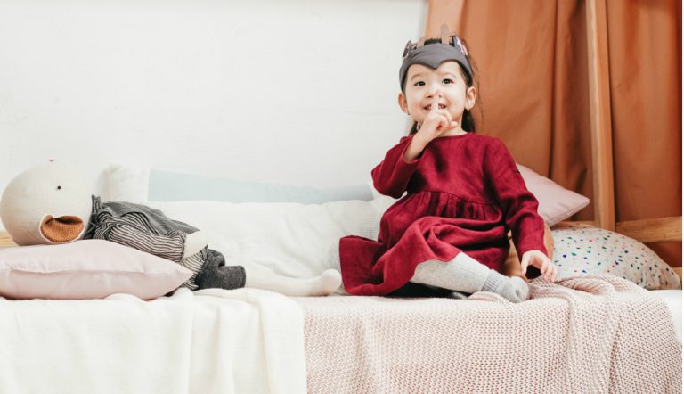 peuter wil niet gaan slapen / meisje zit op bed en maakt ondeugend gebaar