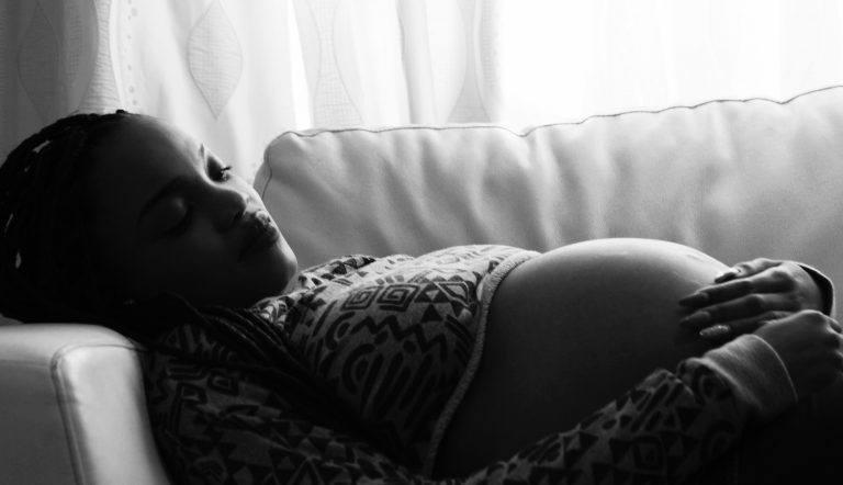 Zwangere vrouw die op de bank ligt en last heeft van zwangerschapskwaaltjes