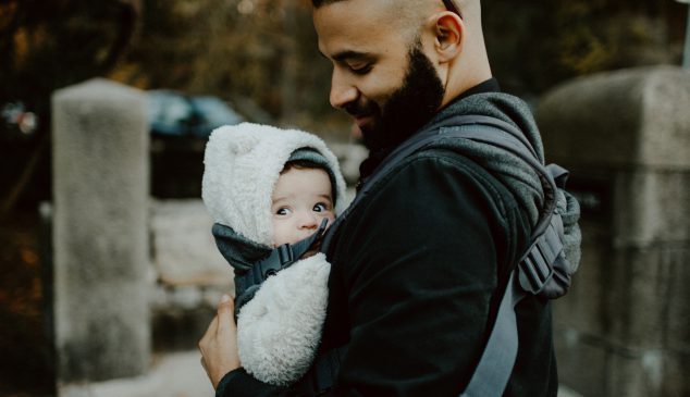 Vader met baby in draagzak die checkt of de temperatuur van de baby niet te warm of te koud is