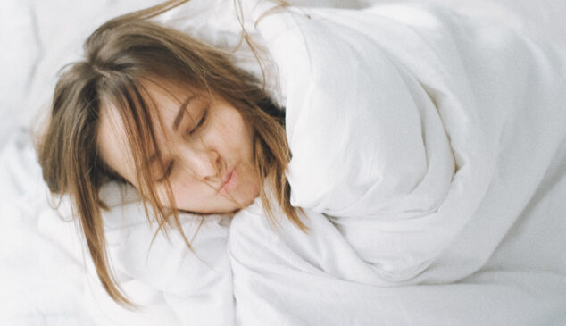 Vrouw die in bed ligt in de dekens gewikkeld omdat ze het koud heeft