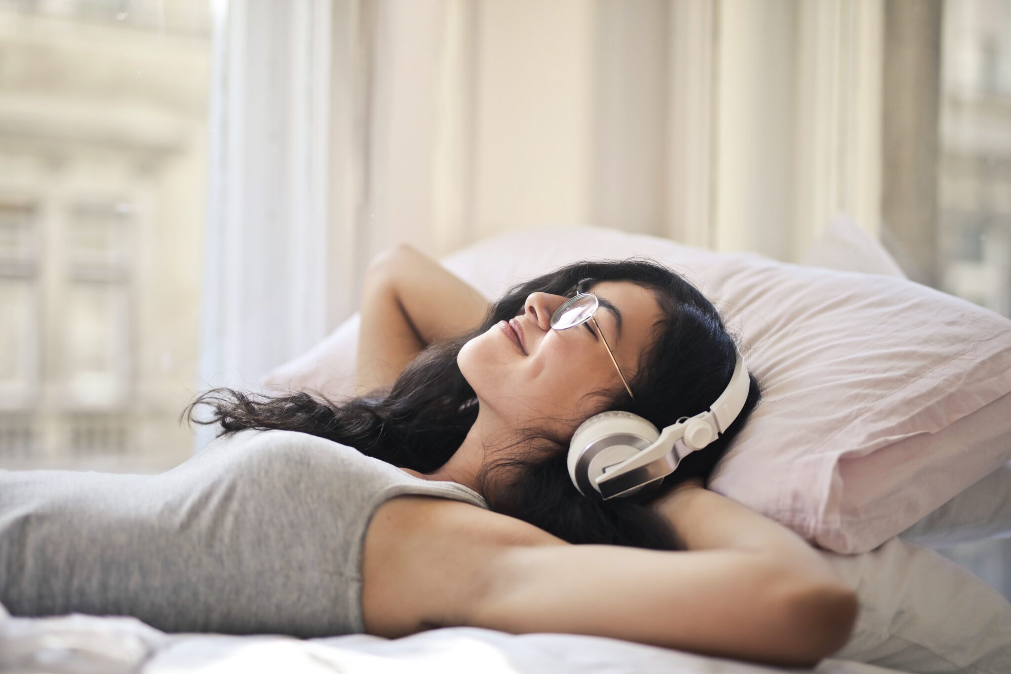 Vrouw met koptelefoon op in bed die naar een luisterboek luistert