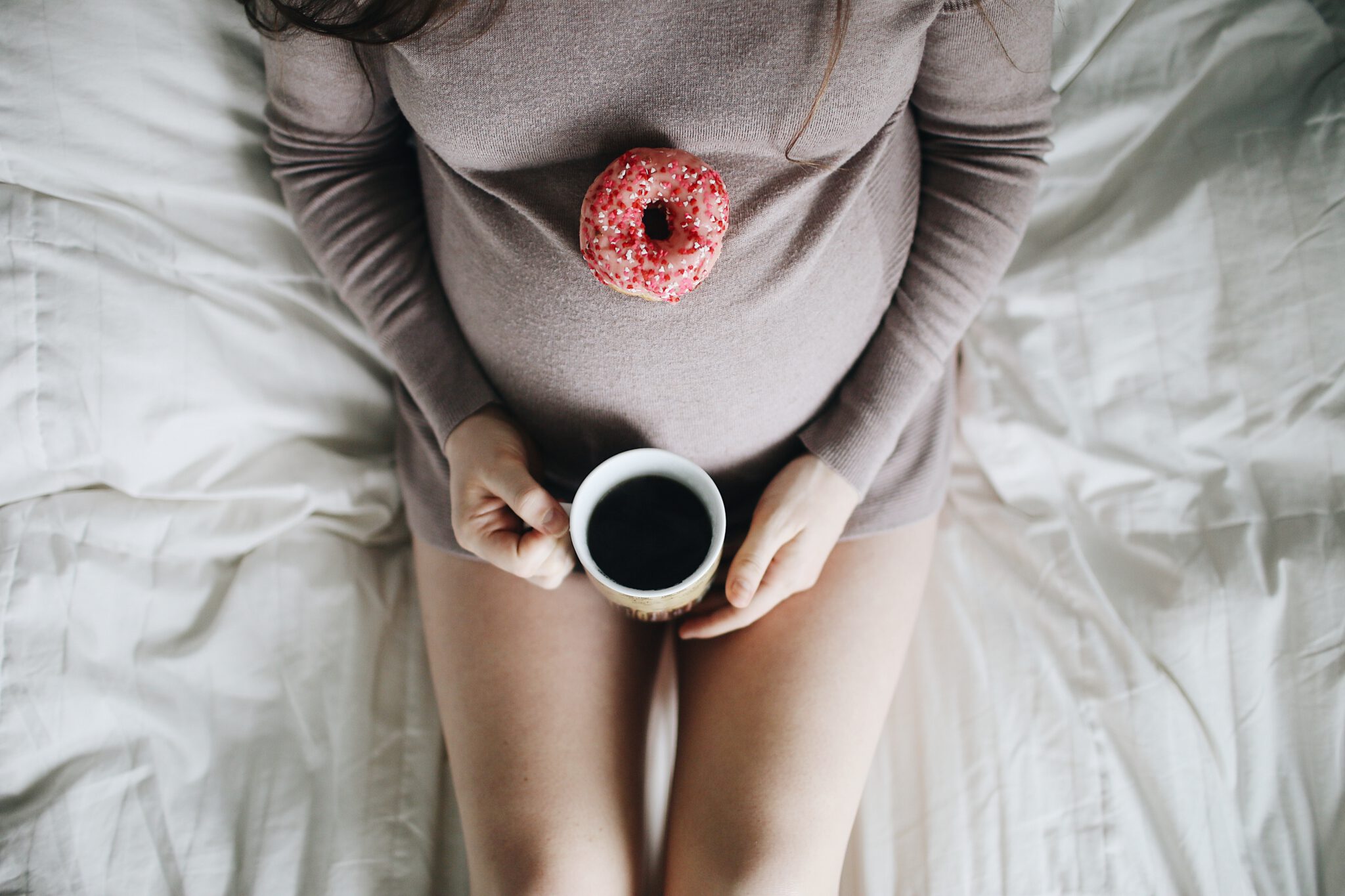 vrouw die met een kopje koffie en een donut op haar zwangere buik zit te genieten zwanger beter niet eten