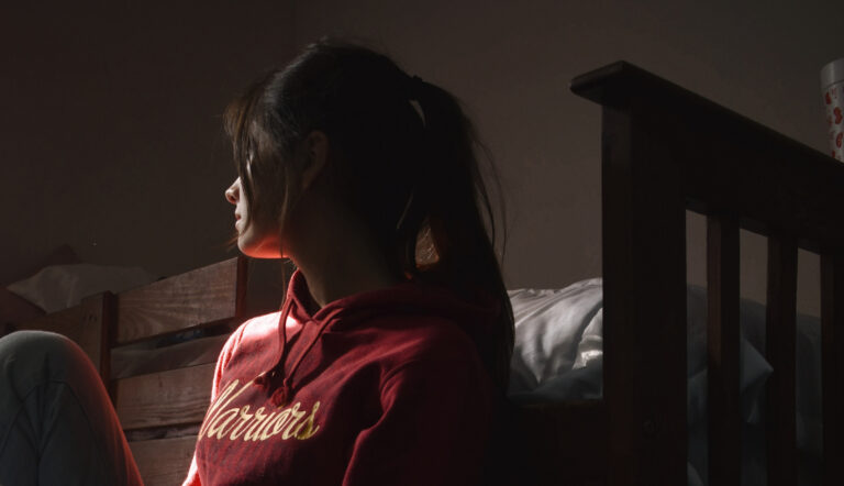 Vrouw die in het donker zit en naar het licht kijkt omdat ze burn-out signalen heeft