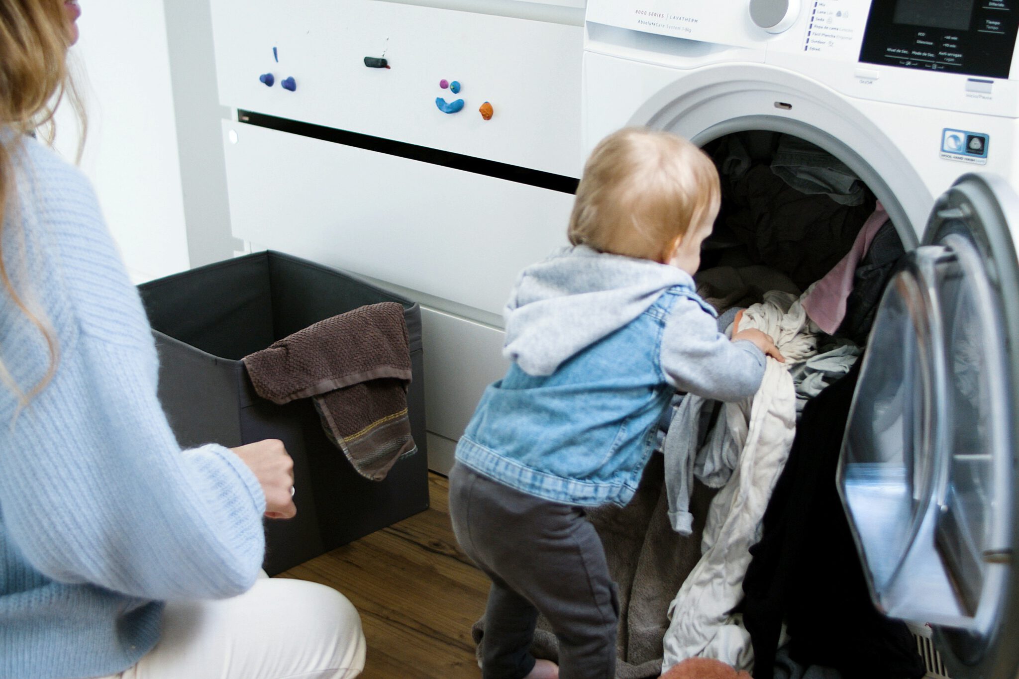 Kindje die de was in de wasmachine doet, terwijl haar ouders deze moeten schoonmaken omdat hij stinkt