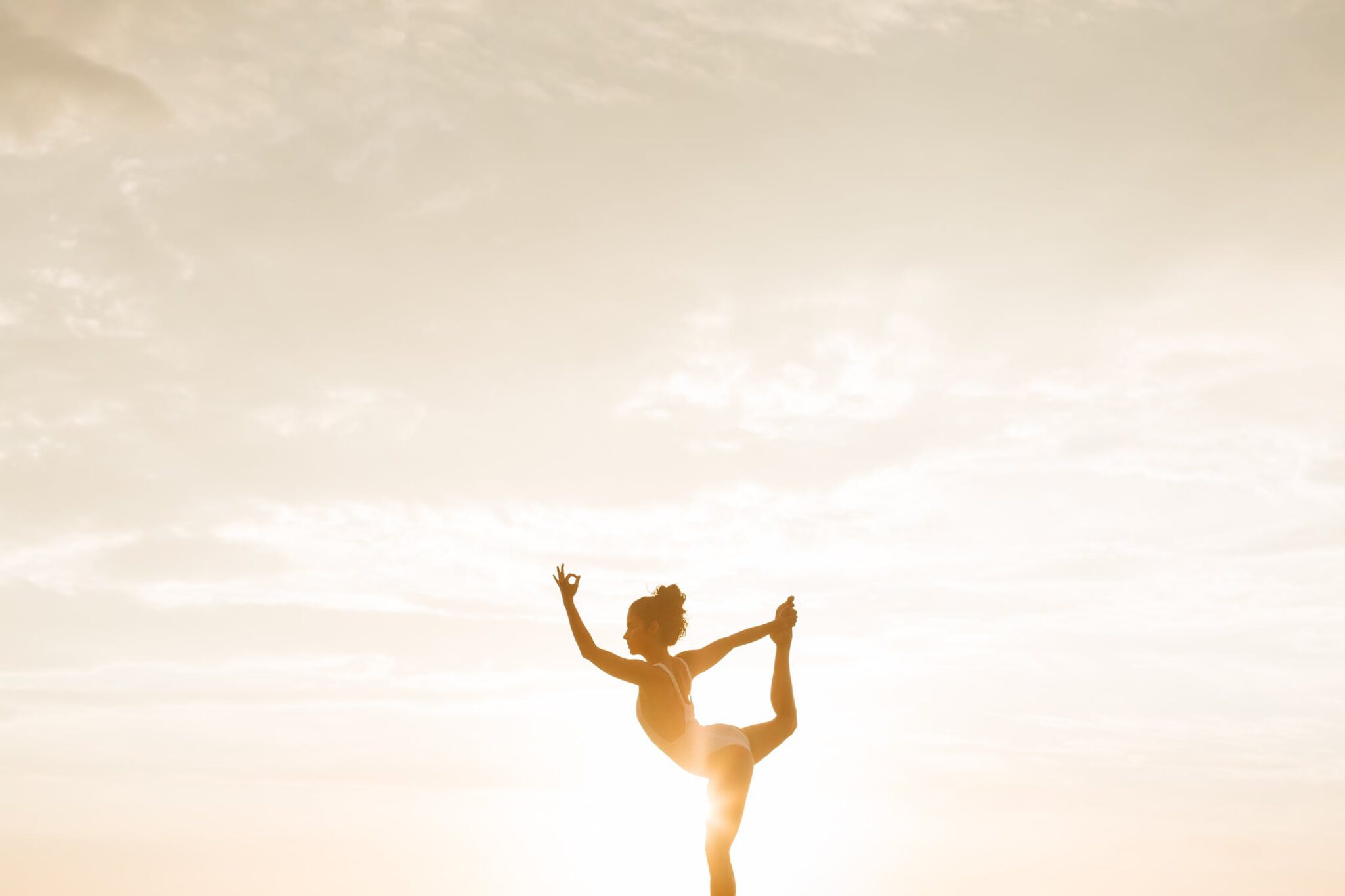 Een vrouw die fertility yoga doet en op 1 been staat tegenover de zonsondergang