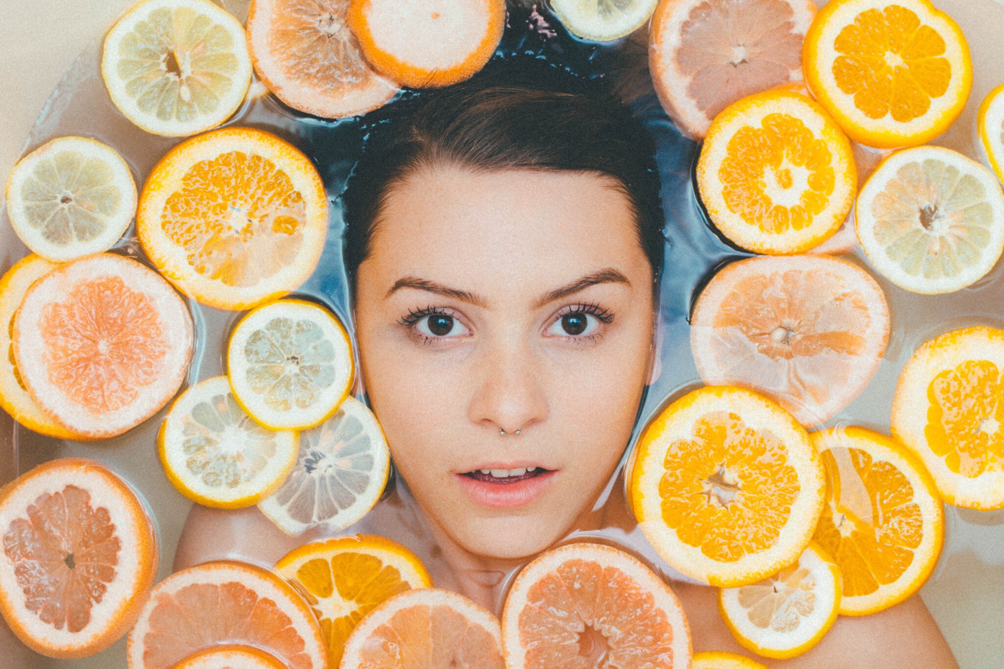 Gezicht van vrouw omringt door citroenen en grapefruit: Vitamine C voor je huid