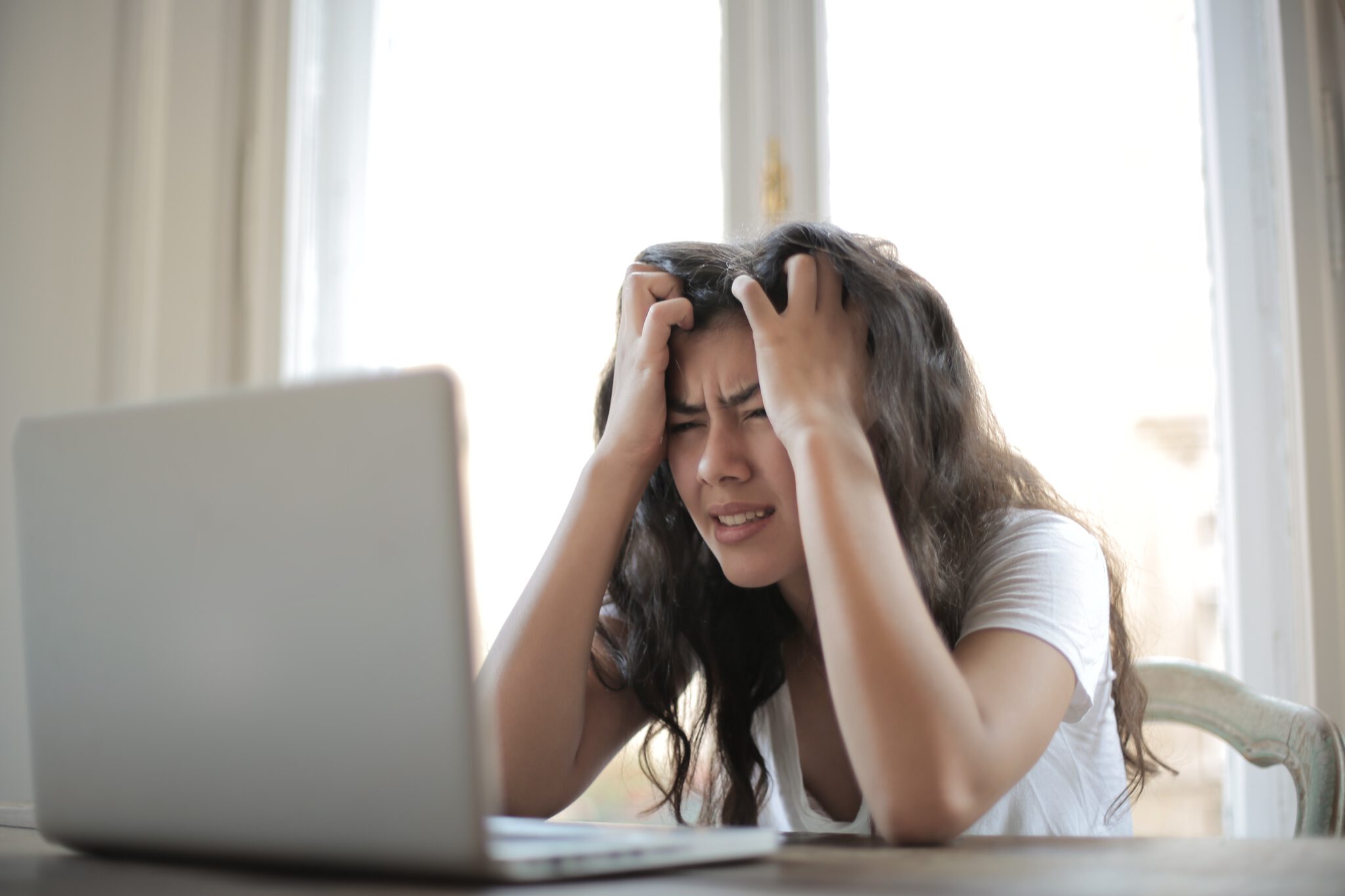 Vrouw zit met handen in het haar gefrustreerd voor haar laptop (en kan tips voor stressbestendigheid goed gebruiken)