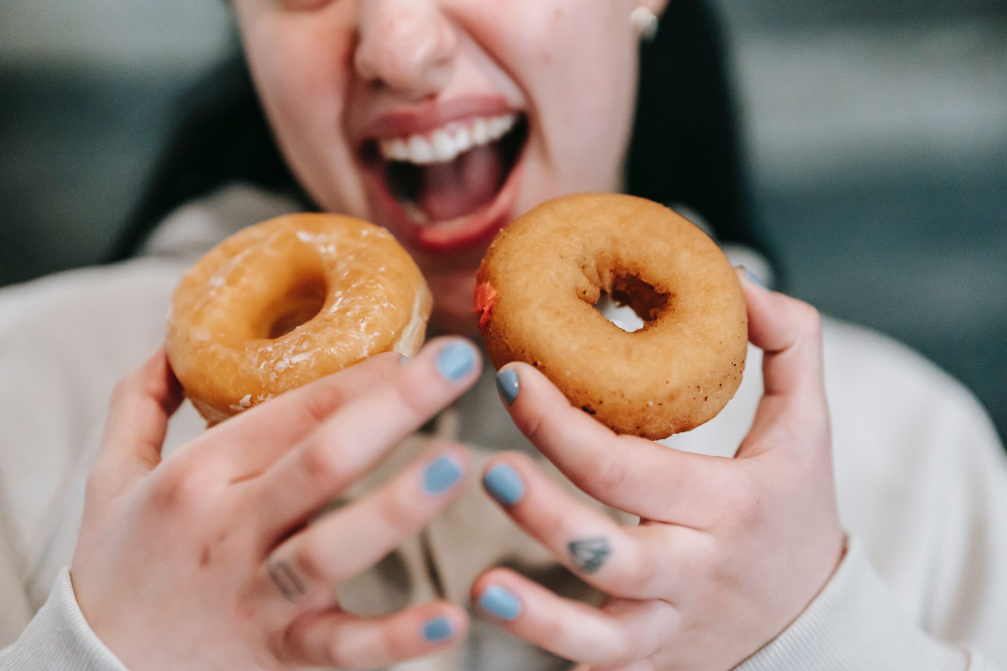 vrouw houdt twee donuts voor haar mond, alsof ze veel gaat eten: een van de beschamende dingen die we doen