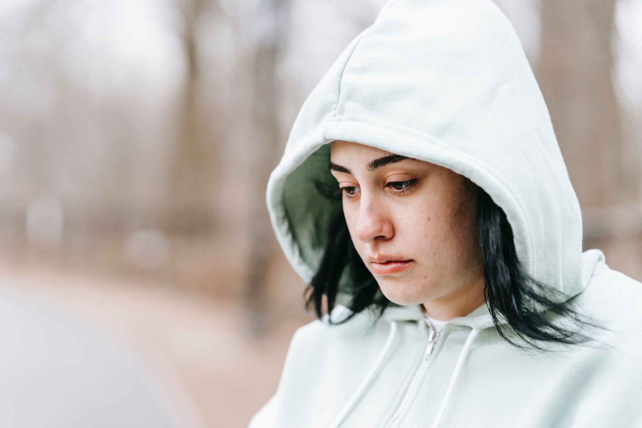 Vrouw met hoodie kijkt verdrietig omlaag, ze weet niet wat de oorzaken van haar onzekerheid zijn