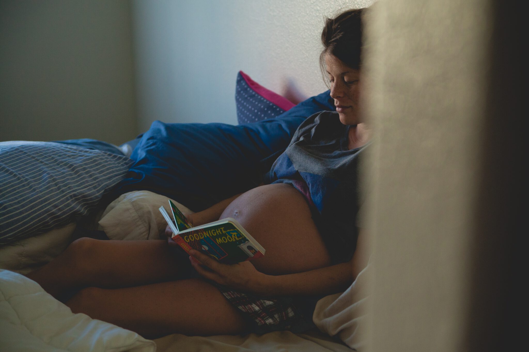 Vrouw met zwangere buik leest boekje en denkt aan babynaam